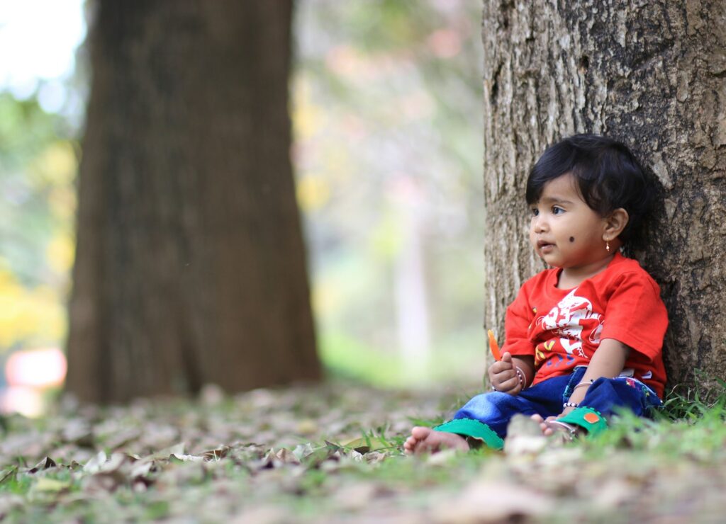 girl in red shirt sitting on ground with dried leaves