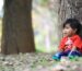 girl in red shirt sitting on ground with dried leaves