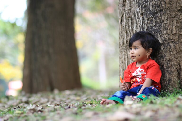 girl in red shirt sitting on ground with dried leaves